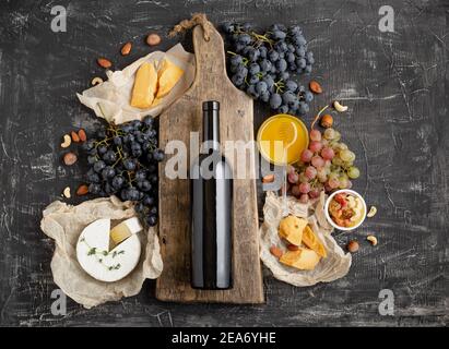 Botella de vino tinto en tabla de madera de corte vintage, moceta de copa de vino. Marco hecho de Gastronomía de diferentes quesos uvas frutos secos de miel. Restaurante