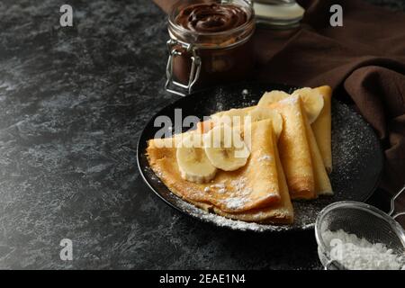 Concepto de delicioso desayuno con crepes con azúcar en polvo y plátano sobre fondo negro ahumado Foto de stock