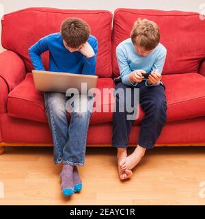 Un niño de 13 años y su hijo de 9 años brother utilizando un ordenador portátil y un ipod touch Foto de stock