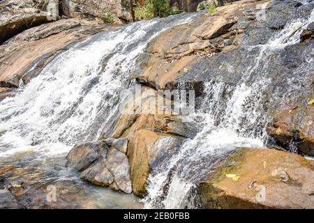 Pequeña cascada que fluye por encima de una gran roca en un famoso lugar cerca de un bosque siempre verde. Foto de stock