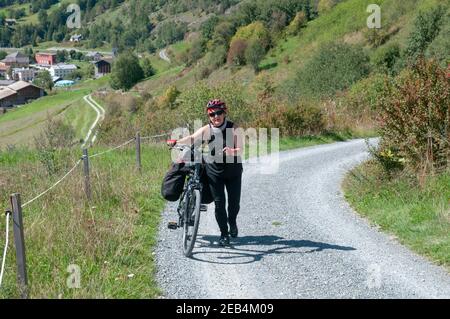 Fatigado ciclista empuja su bicicleta por la empinada subida A Guarda, Suiza Modelo release disponible