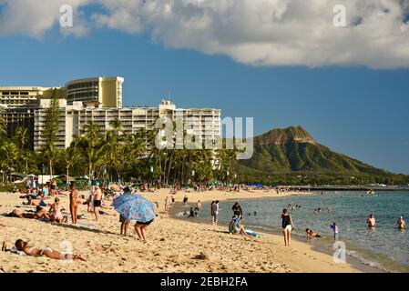 La gente se relaja y toma el sol en la playa de Waikiki, rodeada de complejos turísticos, con cabeza de diamante volcánica en la distancia, en Oahu, Honolulu, Hawaii, Estados Unidos Foto de stock
