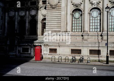 Londres Reino Unido - 13 Feb 2021: Vacía escena callejera de londres con teléfono rojo y sombras largas en el sol de invierno frente al antiguo edificio del siglo 19 Foto de stock