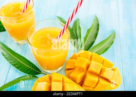 Bebidas refrescantes para el verano, dulce frío y agrio exótico jugo de mango tropical con cubitos de hielo en los vasos en la mesa de madera azul claro Foto de stock