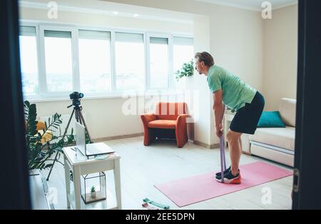 El hombre caucásico está haciendo ejercicios de fitness con cámara en casa llevar ropa deportiva