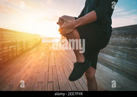Hombre joven sano calentando y estirando las piernas antes del entrenamiento al aire libre