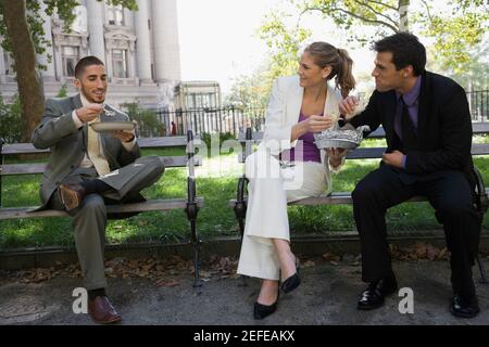 Tres ejecutivos de negocios comiendo comida en los bancos del parque Foto de stock