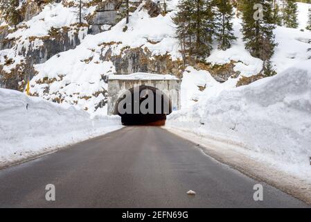 Entrada de un túnel a lo largo de una carretera de montaña que corre entre paredes de nieve arada en invierno