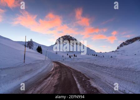 Camino vacío y sinuoso de paso de montaña que corre entre las paredes de la nieve En los Alpes europeos al atardecer en invierno Foto de stock