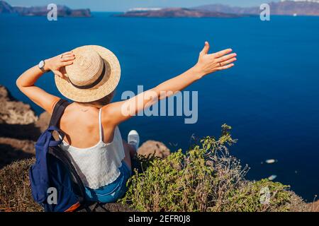 Mujer viajera sentada en el borde de la roca mirando Caldera desde Akrotiri, isla de Santorini, Grecia. Feliz turista relajante durante las vacaciones de verano. Tour Foto de stock