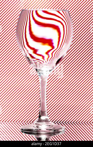 refracción de luz por una copa de vino sobre un fondo rojo y blanco rayado. Arte abstracto del vidrio Foto de stock