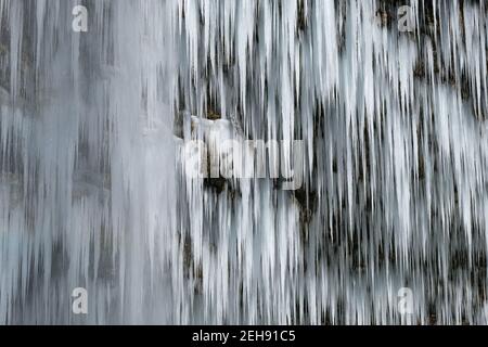 Hermosas y largas icículas de una cascada congelada. El agua fluye y se cae y el hielo gotea en una cueva de montaña oscura y de eery frío Foto de stock