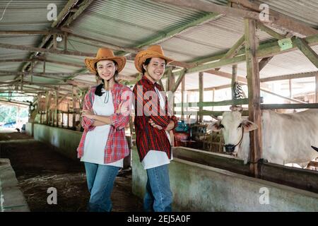 un niño sonriente y una chica con un sombrero se levantan para volver en las manos cruzadas pose en una vaca granja estable