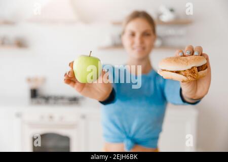Niña caucásica joven haciendo la elección entre la hamburguesa de comida rápida y la manzana verde. Concepto comida vegetariana saludable.