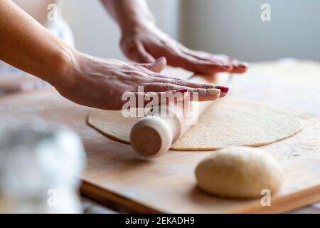 Mujer rodando la masa en la tabla de corte con el rodillo a hacer croissants en la cocina