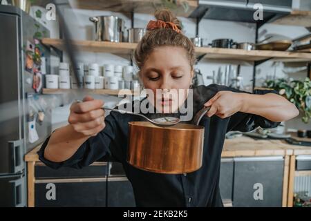 Joven chef degustación de sopa de broth mientras está de pie en la cocina