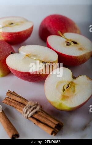 Manzanas enteras y cortadas con bastones de canela sobre fondo de mármol.