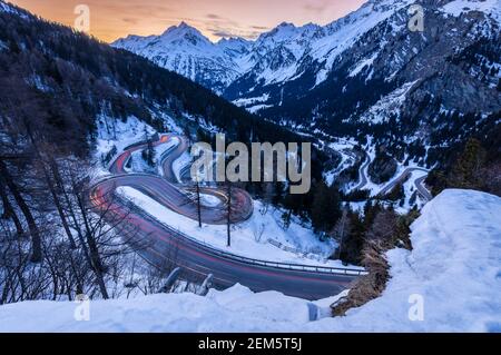 Coches ligeros senderos en las curvas sinuosas de Maloja paso carretera en invierno al atardecer, Valle de Bregaglia, cantón de Graubünden, Engadin, Suiza. Foto de stock