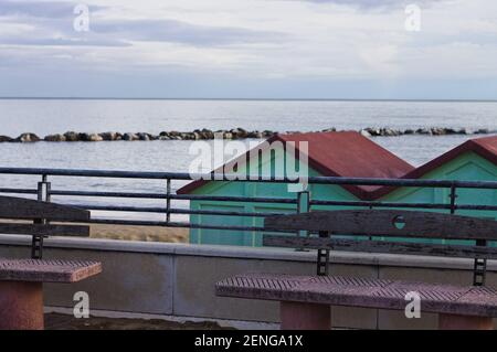 Un par de bancos de hormigón en la acera frente a cabañas de playa en la costa mediterránea (Pesaro, Italia, Europa) Foto de stock