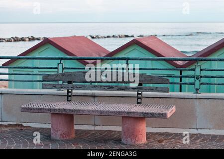 Un banco de hormigón y madera en la acera frente a las cabañas de playa en la costa mediterránea (Pesaro, Italia, Europa) Foto de stock