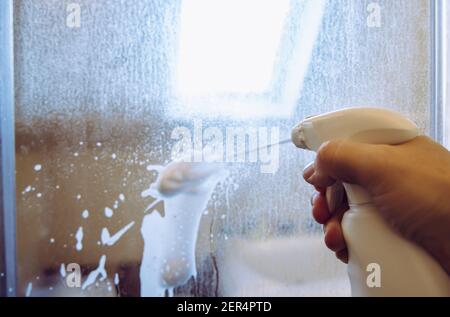 Persona mano usando removedor de cal espuma química. Cubierta de ducha desincrustante puerta de cristal. Trabajo en curso. Foto de stock