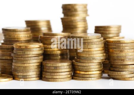 Monedas de color dorado apiladas en pilas sobre fondo blanco Foto de stock