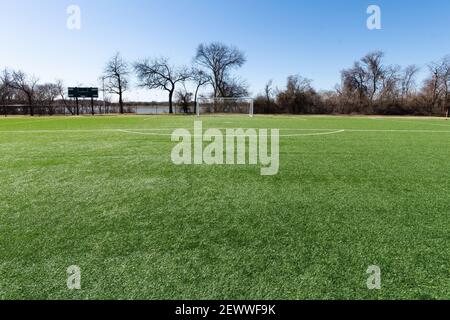 Gol de fútbol en un campo con césped artificial en un parque urbano con árboles y un lago en el fondo.