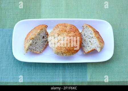 Dos muffins de semilla de amapola de limón en un plato blanco, uno cortado por la mitad Foto de stock