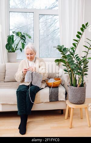 Una mujer mayor durante un encierro, se dedicaba a tejer sentado en el sofá en casa. Foto de stock