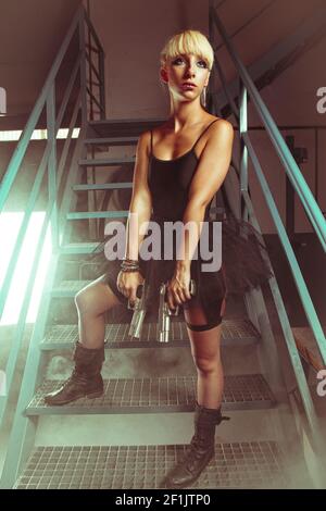 Chica rubia con pistolas en una fábrica abandonada. cosplayer, acción y peligrosa mujer Foto de stock