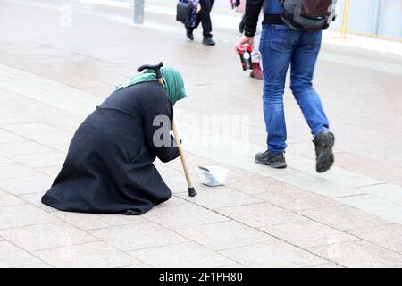 Mendigo vieja mujer pide limosnas sentadas en una calle de la ciudad. Concepto de pobreza, personas sin hogar y mendicidad Foto de stock