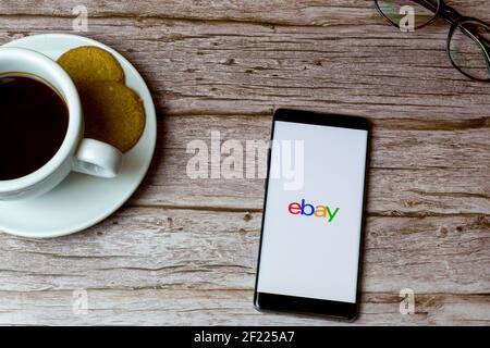 Un teléfono móvil o celular colocado sobre una madera Mesa con una aplicación Ebay abriendo también un café y.. gafas Foto de stock