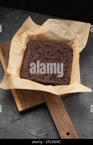 Brownies sin recortar con gotas de chocolate en papel de hornear en la oscuridad fondo de yeso vista de ángulo alto Foto de stock