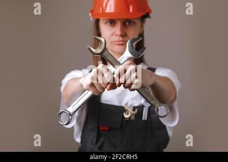 mujer ingeniera en un uniforme y casco de seguridad con dos llaves cruzadas en sus manos y mostrando en cámara. Igualdad entre hombres y mujeres. Repa