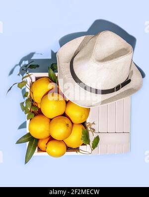 Naranjas frescas con hojas en una caja de madera y sombrero de verano sobre fondo azul. Alimentos saludables de temporada. Vitamina natural C. envases de frutas ecológicos.