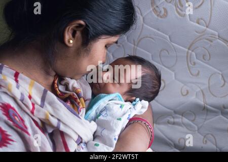 De cerca cara de un lindo recién nacido niño besado por su madre sosteniendo en su regazo madre. Un niño pequeño y dulce de un mes. Etnia India.