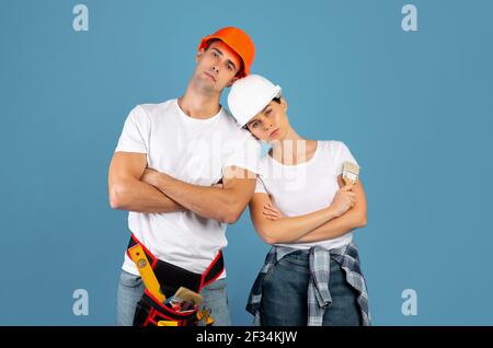 Hombre cansado y mujer en el casco duro agotado después de la reparación Cabezas inclinadas Foto de stock