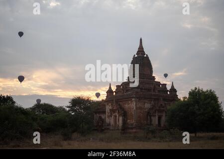 BAGAN, NYAUNG-U, MYANMAR - 2 DE ENERO de 2020: Unos cuantos globos aerostáticos se elevan detrás de un templo histórico de pagoda durante el amanecer temprano por la mañana