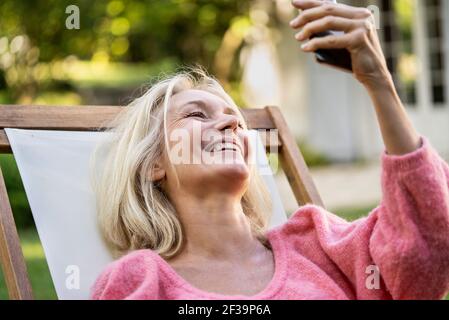 Primer plano de una mujer madura sonriente con videollamada en el smartphone del patio trasero