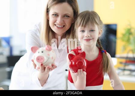 Mujer doctor y niña sosteniendo bancos piggy Foto de stock