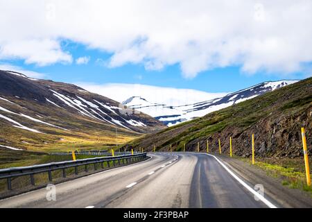 Vista de las montañas de Sulur cubiertas de nieve al oeste de Akureyri con cielo azul durante el soleado día de verano y asfalto de carretera de circunvalación Carretera pavimentada en Islandia Foto de stock