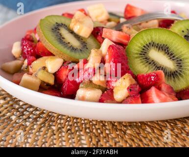 Bocadillos saludables de frutas con fresas picadas, plátanos y kiwis servidos en un plato. Vista aislada y de primer plano Foto de stock