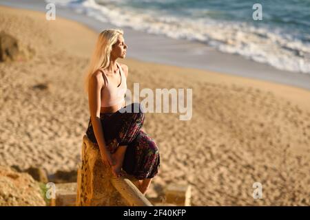 Mujer disfrutando de la puesta de sol en una hermosa playa en Cádiz, Andalucía, España. Mujer joven sentada en hermosas escaleras mirando al mar con luz dorada. Mujer disfrutando de la puesta de sol en una hermosa playa