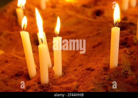 Un grupo de velas de oración encendidas o encendidas en un caja de arena Foto de stock