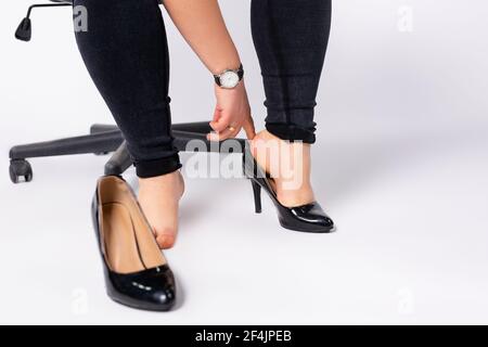 Fotografía recortada de manos femeninas poniendo zapatos negros, moda, laca de tacón en su pie. Mujer de negocios con zapatos formales la oficina, fondo gris Fotografía de stock - Alamy