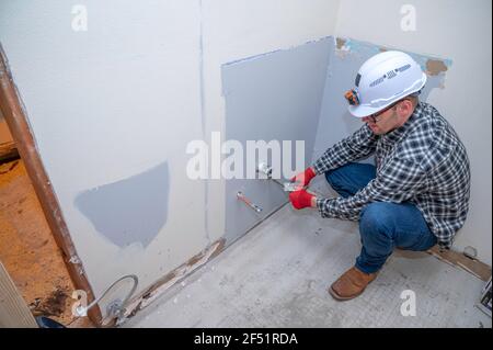 Fontanero instalando nuevas tuberías en el baño durante el proyecto de remodelación de la casa Foto de stock