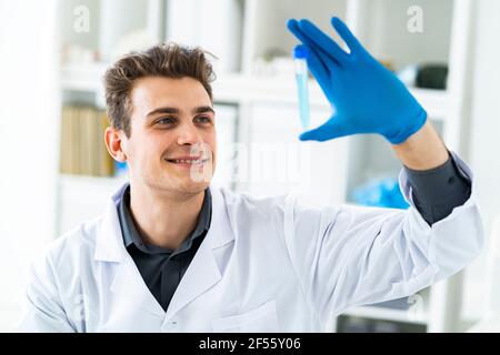 Sonriente hombre científico examinando líquido en el tubo de ensayo