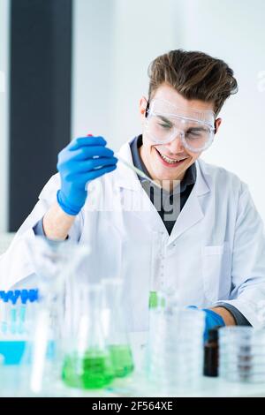 Sonriente hombre científico sosteniendo la pipeta mientras trabaja en el laboratorio