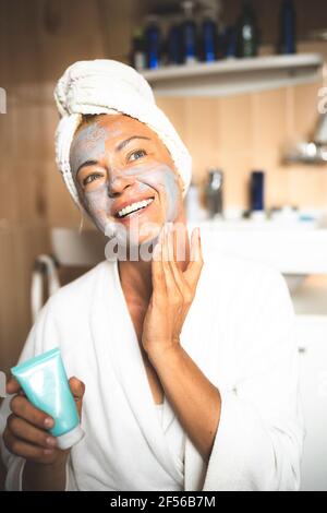 Mujer madura en albornoz aplicando crema de manos para hidratar las manos  después de la ducha