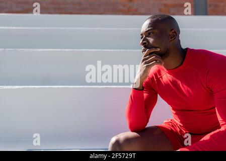 Hombre negro atlético en sportswear sentado en escaleras mirando hacia fuera con cara seria. Espacio de copia
